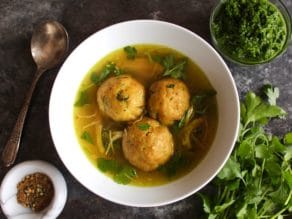 Yemenite matzo ball soup with three large matzo balls in a white bowl on a silver tray.