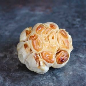 Head of roasted garlic with exposed cloves on grey countertop.