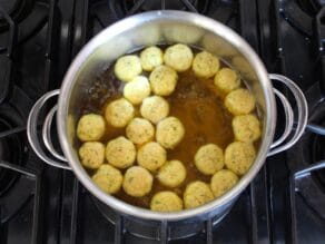 Overhead view of floater matzo balls starting to cook on top of a pot of simmering broth on stovetop.