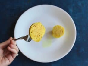 A fluffy matzo ball cut in half, hand with a fork showing half the matzo ball to camera.