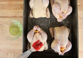 Brushing olive oil over Cornish hens.