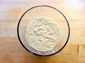 Sourdough starter in a glass jar on a wooden cutting board.