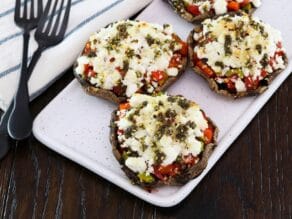 Horizontal shot - Four beautiful stuffed portobello caps with goat cheese on a platter, with a linen towel and two forks beside them.