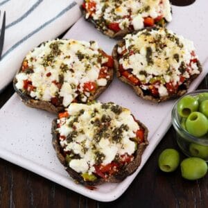 Horizontal shot - Four beautiful stuffed portobello caps with goat cheese on a platter, with green olives and a linen towel beside them.