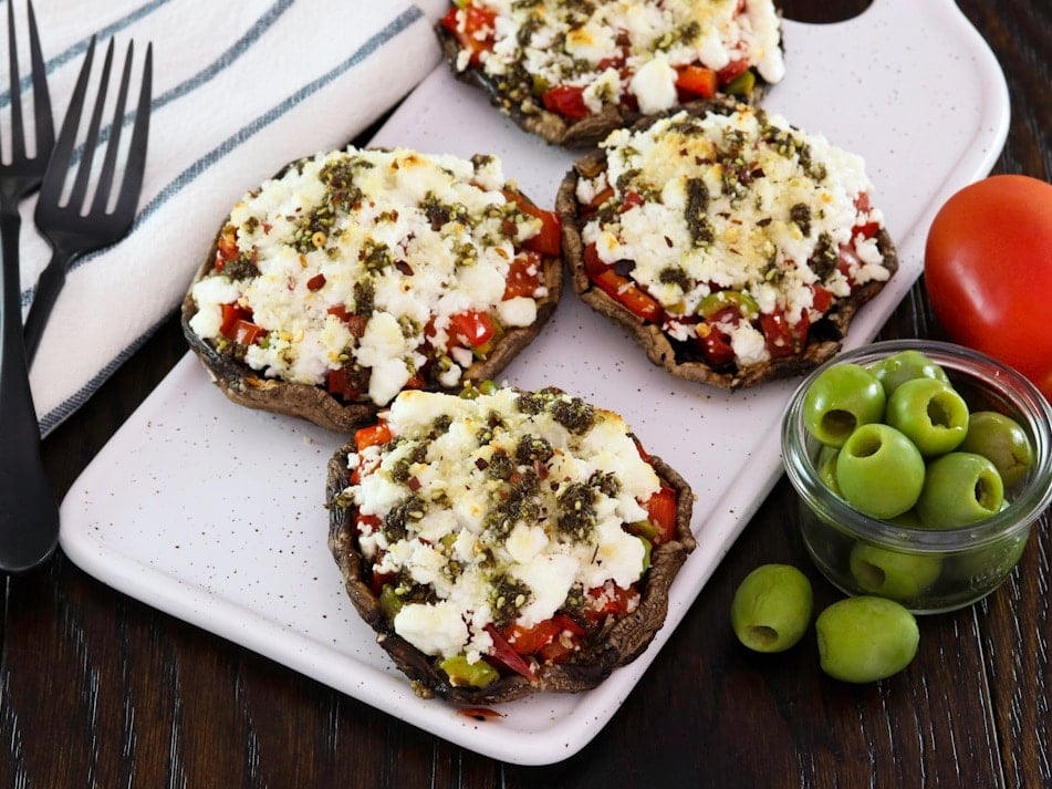 Horizontal shot - Four beautiful stuffed portobello caps with goat cheese on a platter, with green olives and a linen towel beside them.