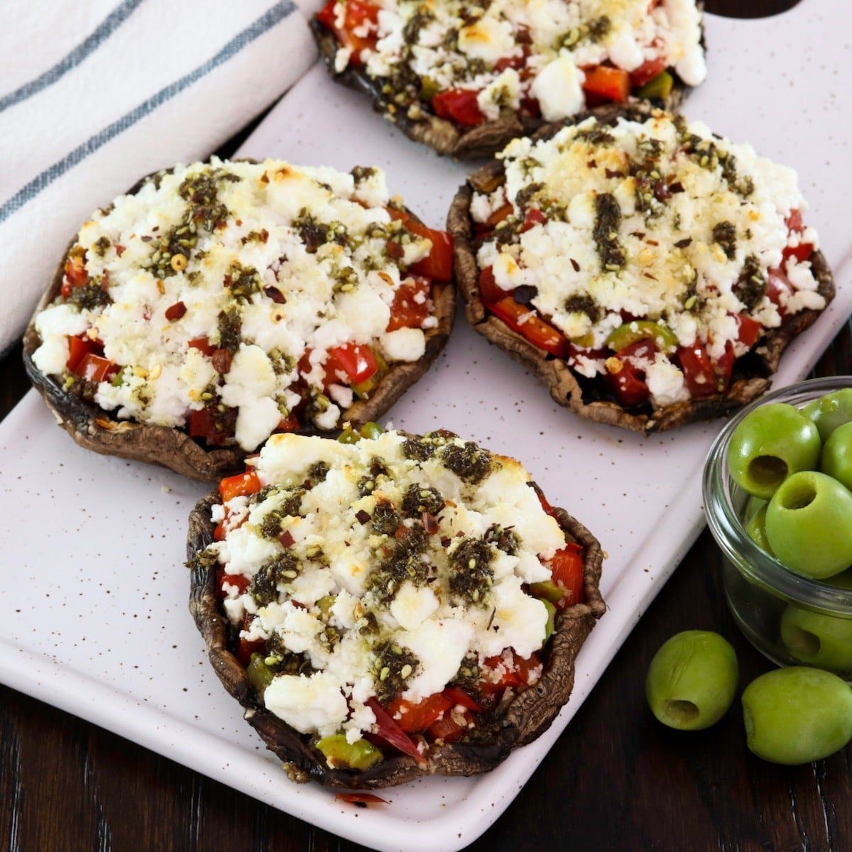 Featured square shot - Four beautiful stuffed portobello caps with goat cheese on a platter, with green olives and a linen towel beside them.