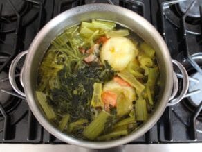 Cooked chicken stock with softened cooked vegetables floating on the surface.