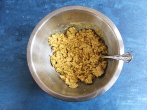 Matzo ball batter being stirred by fork in a stainless bowl on blue countertop.