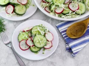 Horizontal shot of two plates of crunchy pickled salad, off to the right is a large bowl of the same salad. A wooden spoon sits on top of a blue and white striped napkin just beneath the bowl.