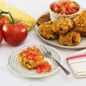 Horizontal shot of panko corn and pepper schnitzel, topped with tomato relish on a small plate with a fork. In the background there is a plate to the right with more schnitzel and relish, to the left there are whole tomatoes.