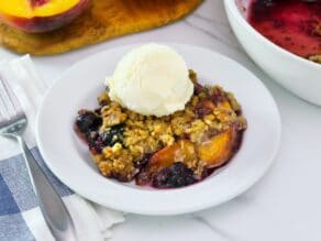 Close-up image - a dish of peach and blueberry crisp topped with a scoop of vanilla ice cream.