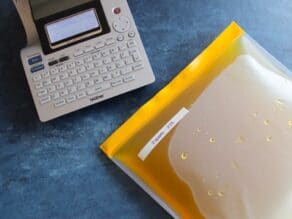 Silicone reusable bag filled with chicken stock and sealed, labeled with date, label maker beside.