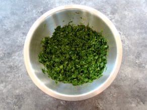 Overhead shot of green herbs - parsley and mint in mixing bowl.