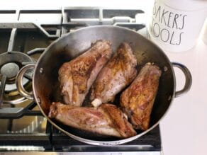 Pan of four lamb shanks browned and seared on stovetop.