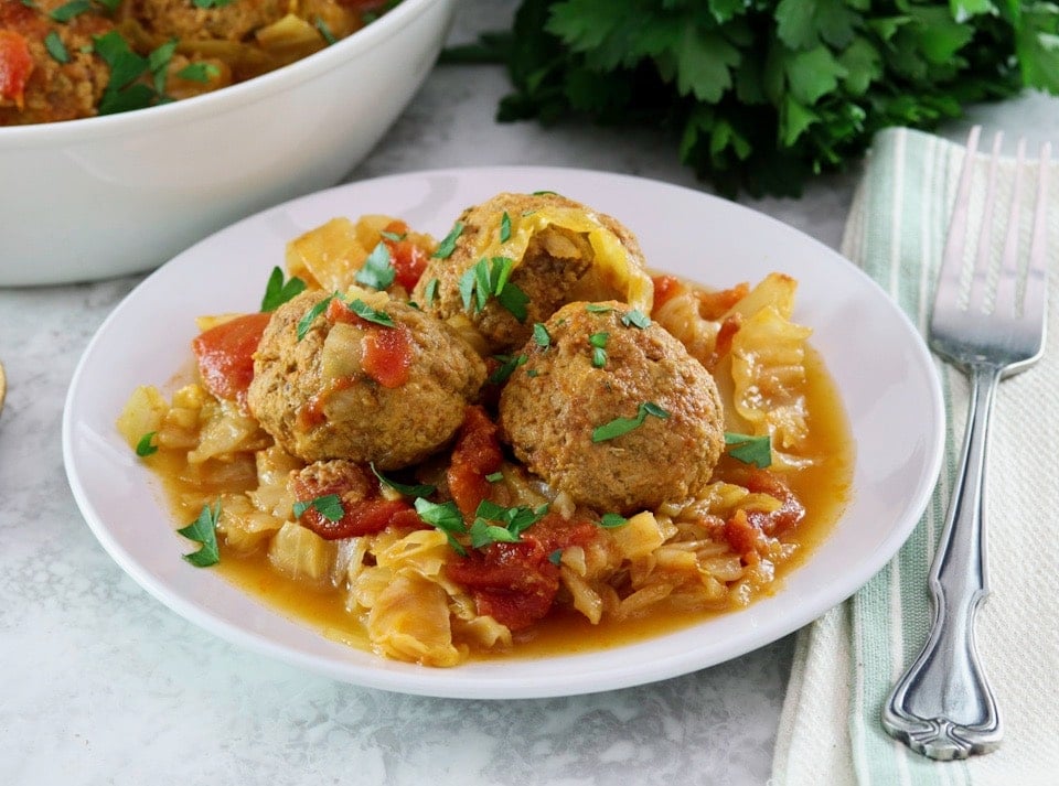 Horizontal image of a white bowl filled with "unstuffed cabbage". A bunch of fresh parsley sits in the back left corner.