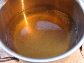 Pot of golden chicken stock glimmering in the light.