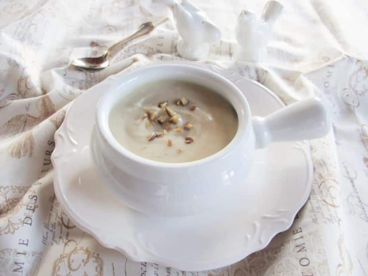 Close-up of Jerusalem Artichoke Soup topped with crushed chestnuts served in a fancy bowl on a fancy table cloth with a spoon