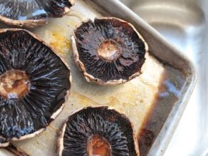 Pouring excess liquid off a baking sheet with roasted portobello caps.