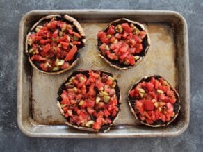 Vegetable-stuffed portobello caps, four on a baking sheet.