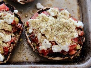 Stuffed portobello caps on a baking sheet sprinkled with nut crumbs.