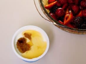 Overhead shot of small white dish filled with creme fraiche, honey, and black pepper. A bowl of mixed berries is in the upper right corner.