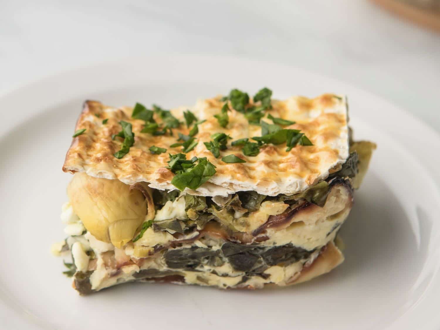 Horizontal shot of a slice of Spinach, Feta, and Artichoke Matzo mina - a layered casserole made with matzo.