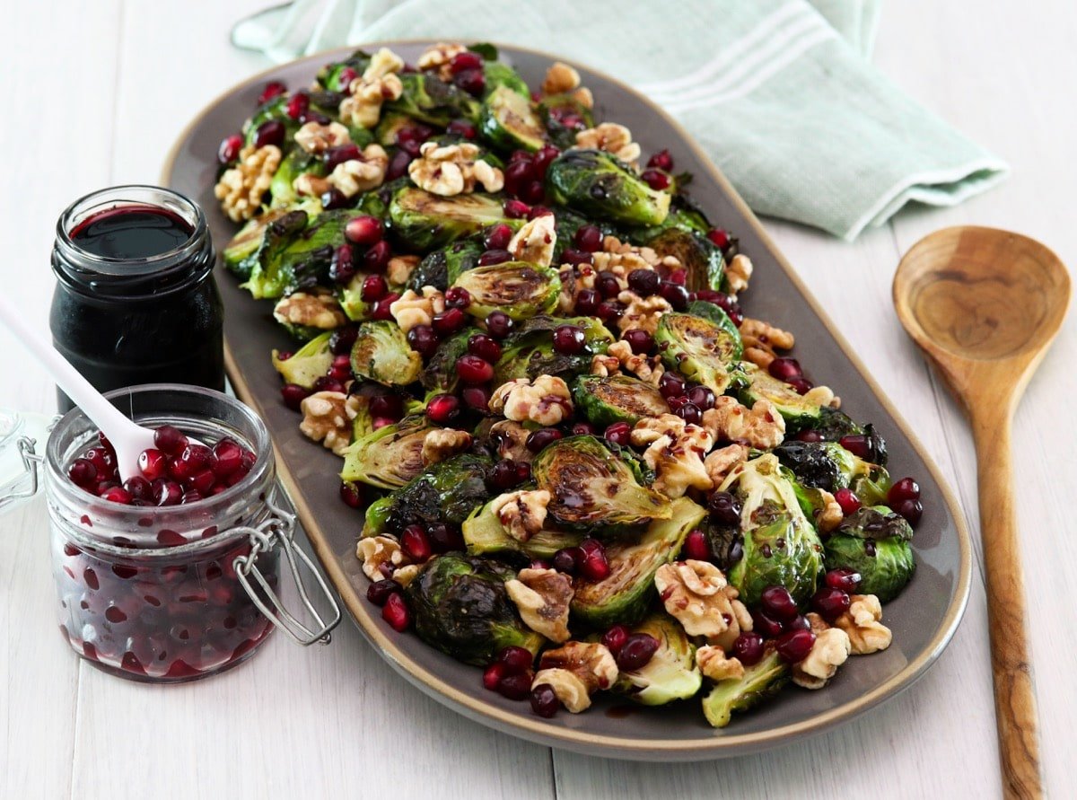 Horizontal shot of a platter filled with roasted brussels sprouts topped with pomegranate molasses.