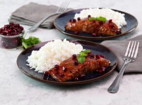 Horizontal shot of two plates holding pomegranate glazed salmon next to a serving of white rice.