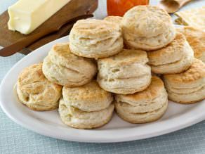 Close-up of Flaky Buttermilk Biscuits stack on top of each other and a block of butter and wooden small knife on the left side