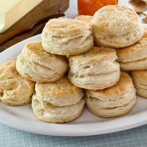 Close-up of Flaky Buttermilk Biscuits stack on top of each other and a block of butter and wooden small knife on the left side