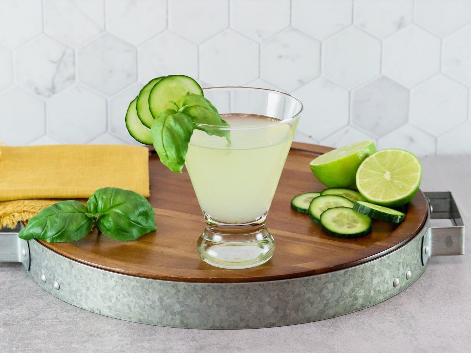 Horizontal shot of a short cocktail glass filled with a pale green drink - a cucumber martini recipe - garnished with slices of fresh cucumber.