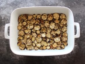 Roasted eggplant slices bottom layer in 2 quart casserole dish on concrete surface.