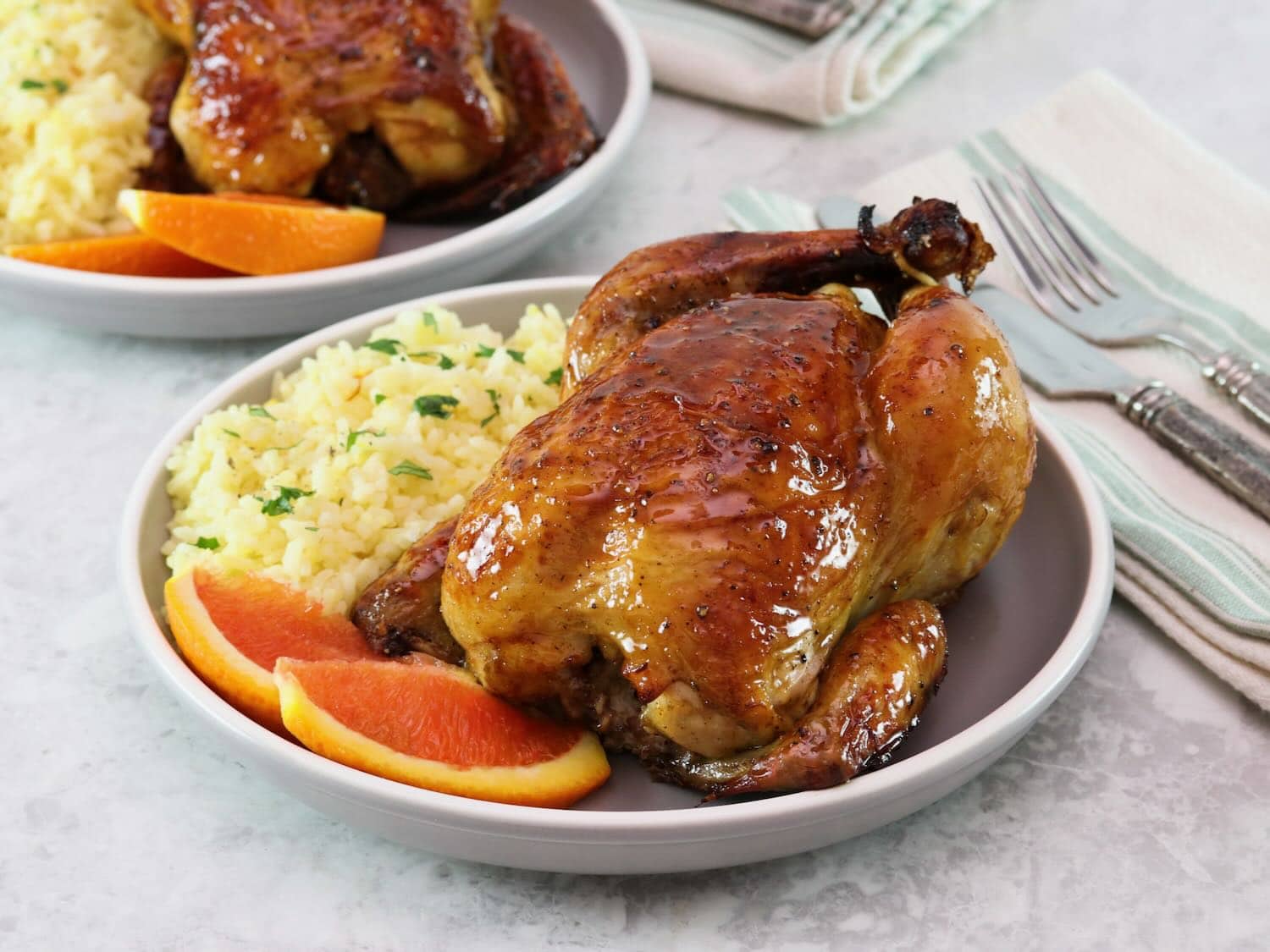 Horizontal shot of a plate containing a citrus marinated game hen on a bed of rice, garnished with fresh orange slices.