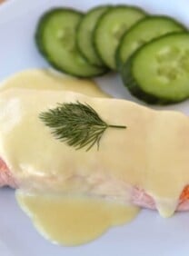 Salmon Mousseline on a white plate with sprig of dill and cucumber salad on the side.