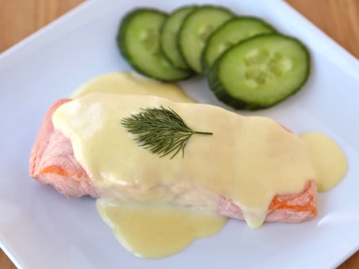 Salmon Mousseline on a white plate with sprig of dill and cucumber salad on the side.