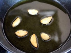 Whole garlic cloves in hot oil in small cast iron skillet, lightly sizzling, turning golden brown and roasted.