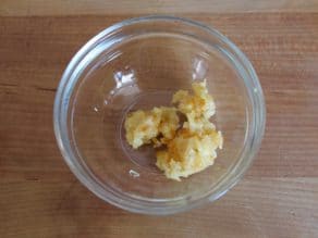 Chopped roasted garlic cloves in small glass bowl on wooden cutting board.