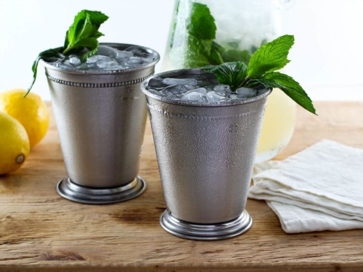 Two glasses of refreshing Sparkling Lemon Mint Juleps summer cocktail topped with mint leaves on a wooden table