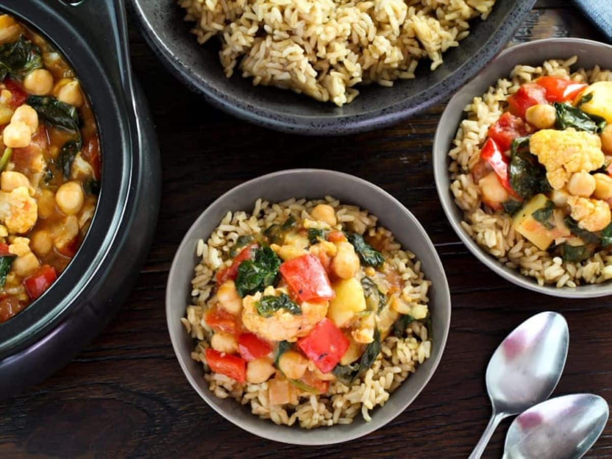 Bowls of rice topped with curried vegetable stew with 2 spoon on the side