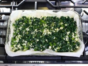 Overhead shot of a sheet of phyllo dough topped with spanakopita filling on a metal baking tray.