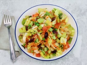 Overhead shot - colorful bowl of salad with cloth napkin and fork on a marble background.