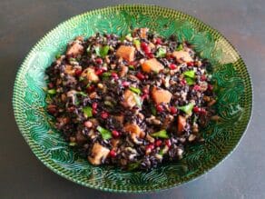 Overhead shot of black rice mixed with butternut squash, chopped fruit and fresh mint in a green decorative bowl.