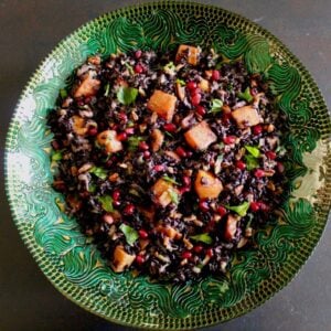 Overhead shot of black rice mixed with butternut squash, chopped fruit and fresh mint in a green decorative bowl.