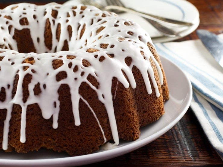 Close-up of a Sour Cream Coffee Cake topped with drizzled cream and served on a white plate