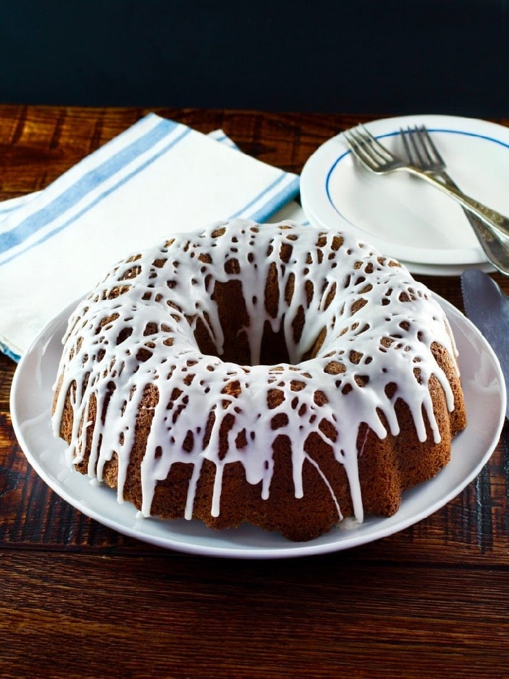 Wide shot of sour cream coffee bundt cake drizzled with white icing, napkin, plate and fork in background.