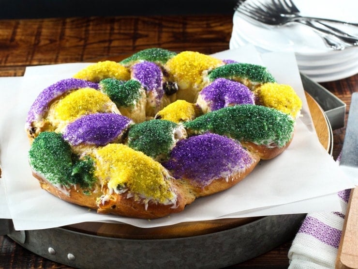 Brightly decorated braided circular King Cake on white parchment with towel in background.