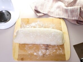 Thick round cylinder of dough on a lightly floured wooden cutting board, linen towel in background.