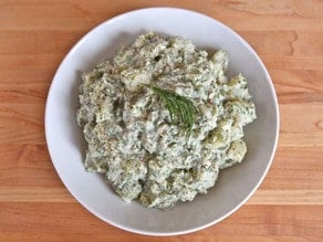 Close-up horizontal shot of potato salad with dill and Dijon mustard on a white plate, garnished with fresh dill.