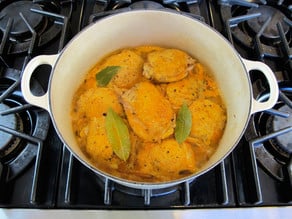 Chicken thighs added to stock in a Dutch oven.