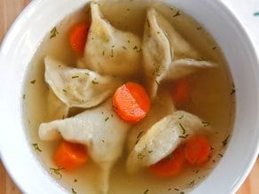 Close-up of chicken kreplach in broth with chopped carrots served on a white bowl